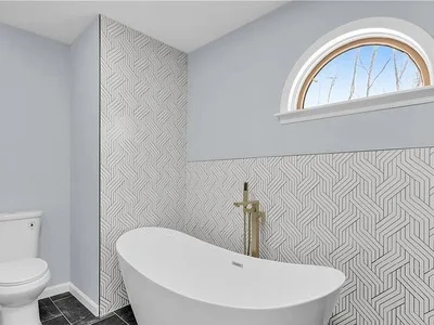 Freestanding soaking tub with geometric tile accent wall and arched window in Malvern, PA