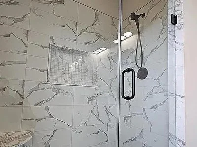 Walk-in shower with large-format marble tile, glass door, and recessed built-in niche in Strafford, PA